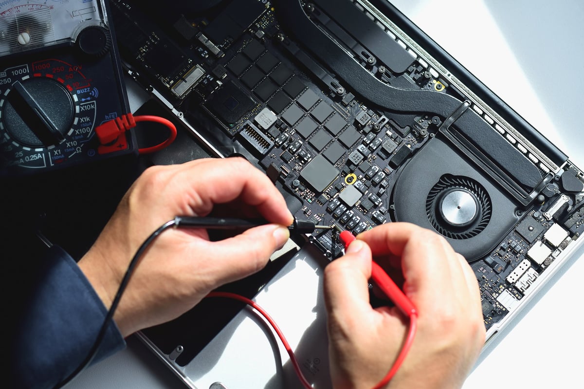 computer technician A laptop motherboard repairman is using an IC meter to find defects on the motherboard to repair on his table.