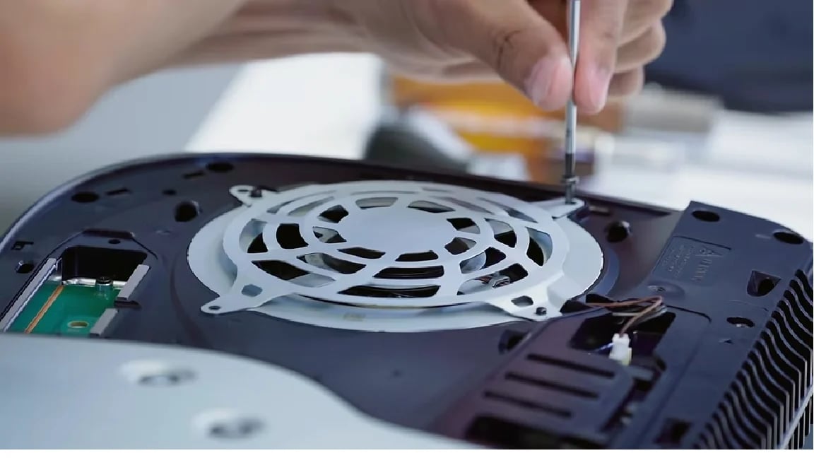 Person using screwdriver to open laptop base panel, revealing internal cooling fan and circuit board components
