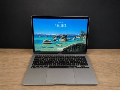 Silver laptop on wooden desk displaying tropical beach scene with turquoise water and rocks on screen