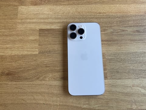 Silver iPhone 13 Pro on wooden surface, showing rear camera system with quad lenses