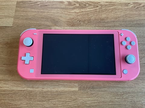 Pink Nintendo Switch Lite handheld gaming console with blue buttons on a wooden surface