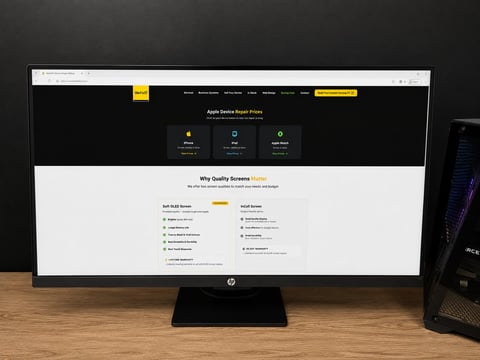 Desktop setup with HP monitor displaying a website, black keyboard, two mice, and wooden desk
