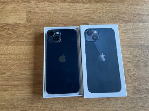 Two iPhone models in white boxes displayed on wood surface, showing back cameras and Apple logos