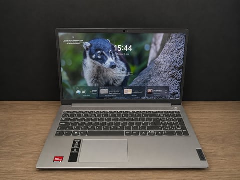 Laptop on wooden desk displaying system information on screen with computer hardware boxes in background