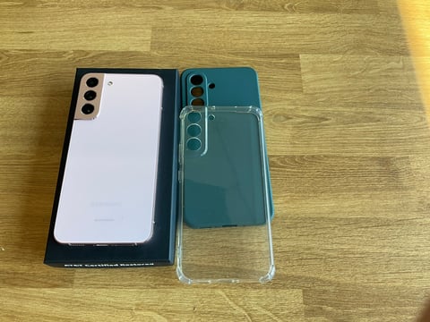Two smartphones on a wooden surface: a white phone in a black box on the left and a teal phone with a clear case on the right
