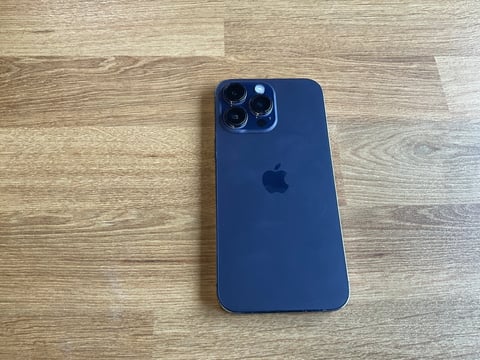 Navy blue iPhone 14 Pro lying on wooden surface, showing rear camera module with multiple lenses